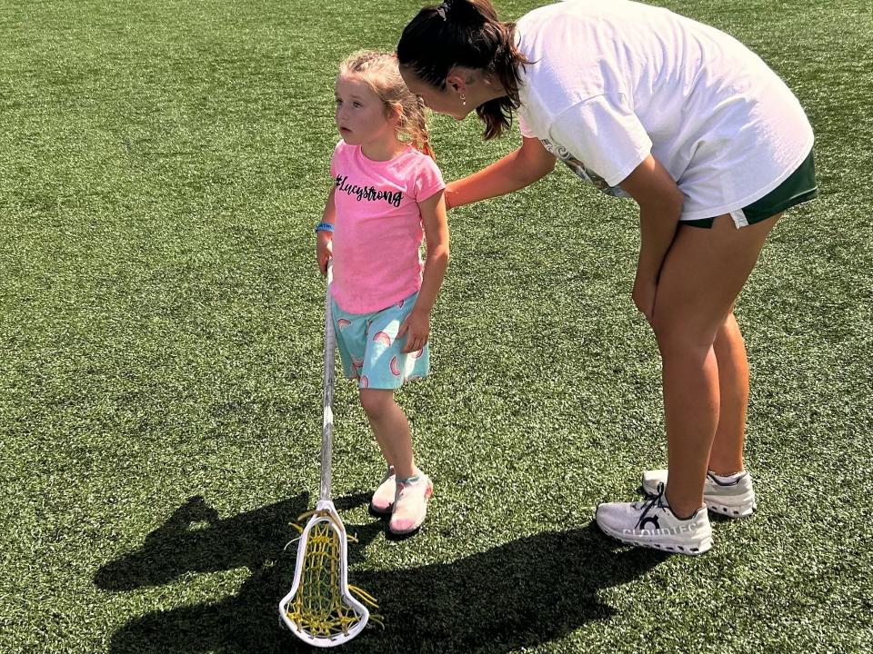 Jacksonville University graduate senior midfielder Quinn Malcom helps 5-year-old Charlotte Donmoyer with some lacrosse fundamentals after the Dolphins' ASUN championship game loss to Coastal Carolina on May 4. Charlotte and her family have grown close with the team since JU adopted Charlotte's sister Lucy, who passed away in September of 2023. The family connected with the team through Friends of Jaclyn, a program that pairs college teams with pediatric cancer victims.