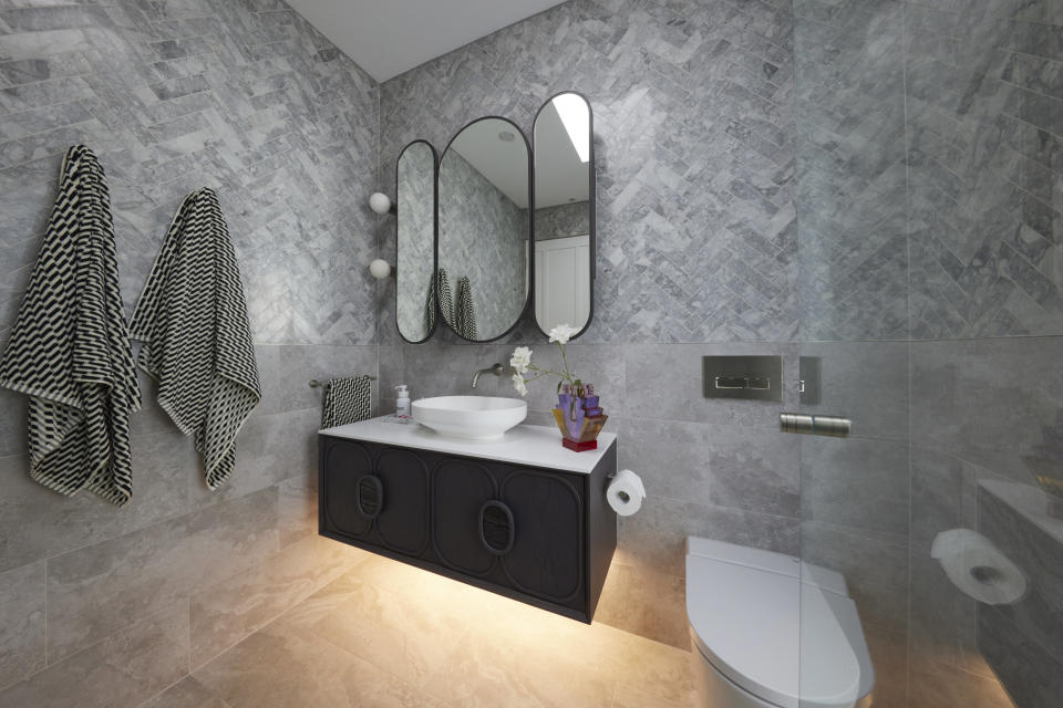 Wide shot of the bathroom, with the vanity, towels hanging on the left wall and toilet to the right. 