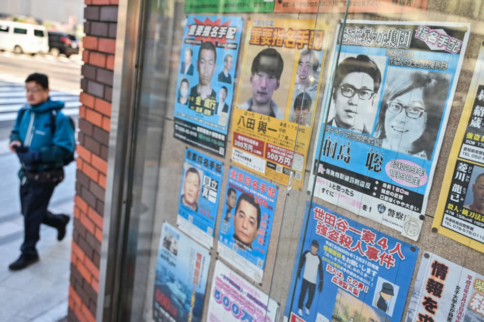 Person walking past a bulletin board with various flyers, some with images of individuals' faces. Text is mostly in Chinese