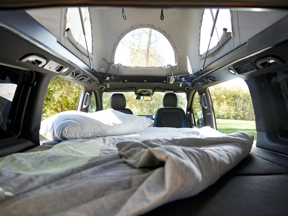 A bed with a blanket, pillows under the pop-top roof.