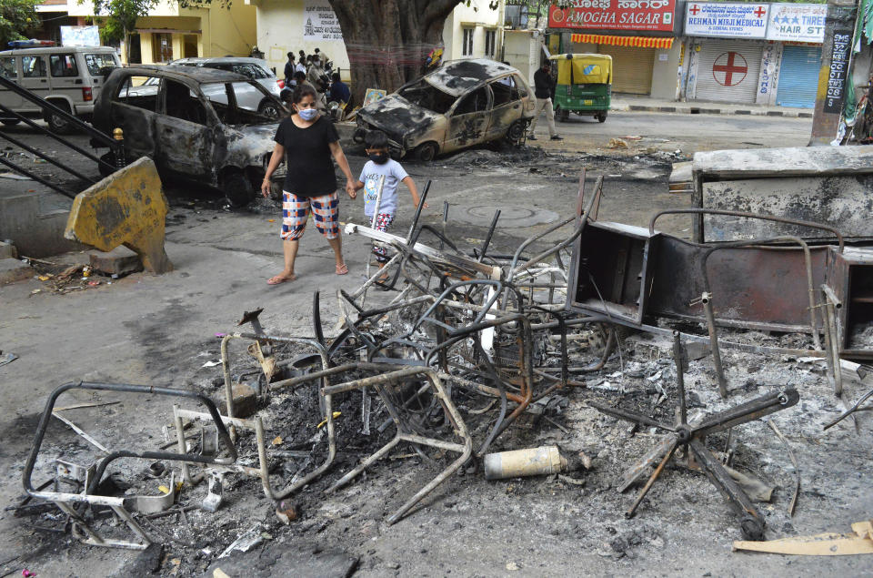 A woman and a child walks past the wreckage of vehicles and furniture burnt during violent protests in Bengaluru, India, Wednesday, Aug. 12, 2020. At least three people have died in the southern Indian city also known as Bangalore after hundreds of demonstrators clashed with the police overnight against a Facebook post considered offensive to Muslims, attacking a police station and setting fire to vehicles, police said Wednesday. (AP Photo)