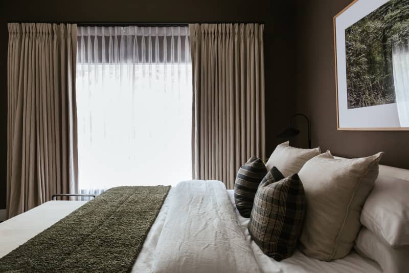 Dark green walls, white tongue and groove with beams, dark green throw blanket, floor to ceiling beige curtains