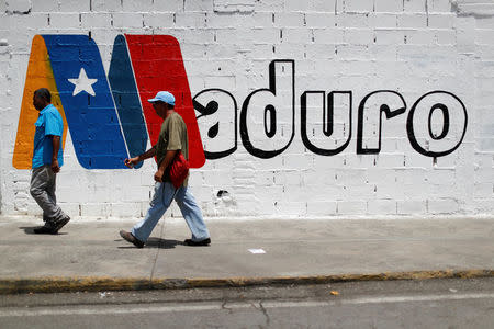 Supporters of Venezuela's President Nicolas Maduro walk past a campaign mural before a rally with him, in Charallave, Venezuela May 15, 2018. REUTERS/Carlos Garcia Rawlins