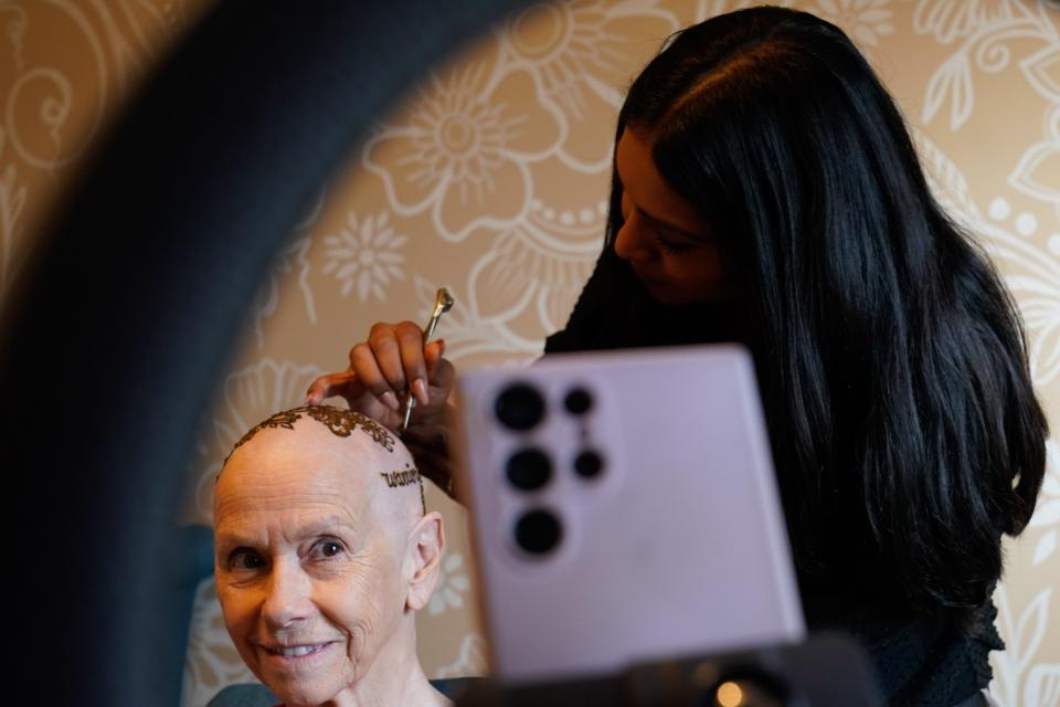 Bernice Schwartzman watches as Vidhi Heiland finishes the letters spelling 'warrior' as part of her henna crown applied Friday morning.