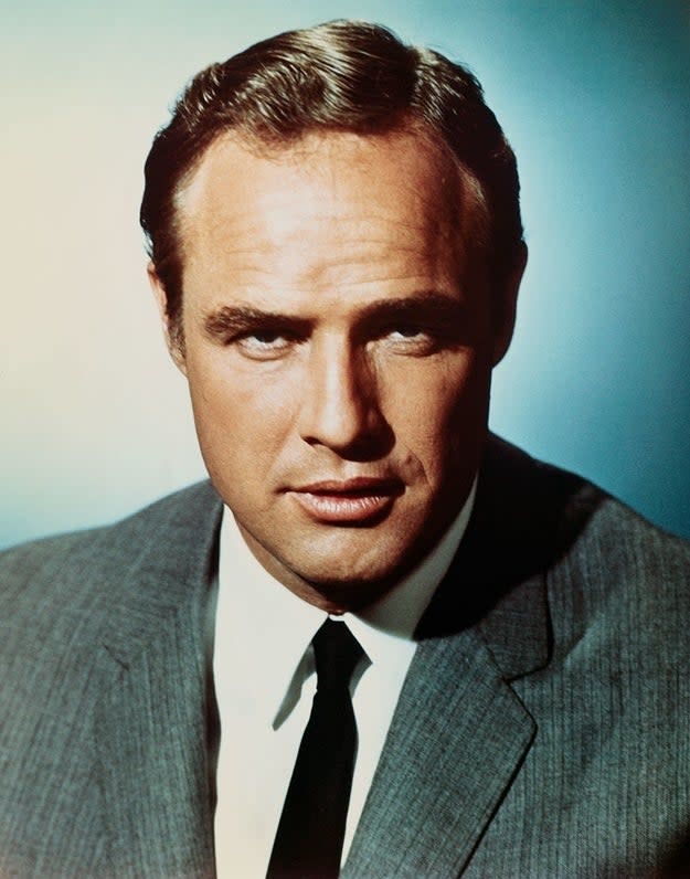 Marlon Brando in a classic suit and tie, looking directly at the camera with a serious expression against a plain background