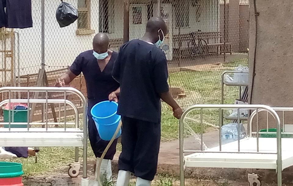 two men outside in scrubs and masks, sanitizing beds of ebola patients with buckets