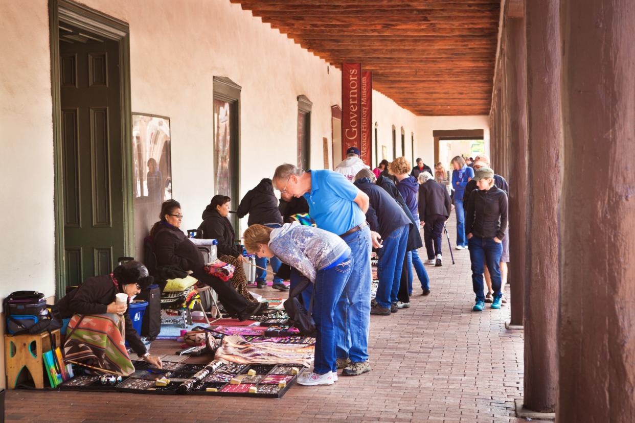 Tourists and pedestrians enjoying and shopping in the arts and crafts outdoor market of the Plaza of Santa Fe, New Mexico.