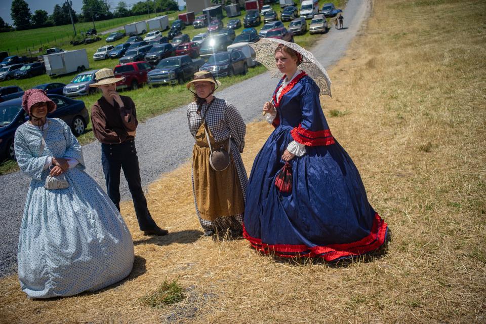 Four people based in 1860s period stand with a parking lot visible in the background.