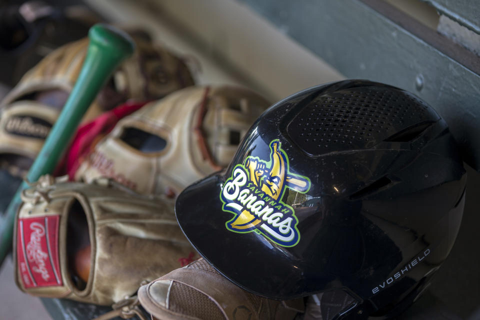 A batter's helmet with the Savannah Bananas logo sits on top of catcher's gear Tuesday, June 7, 2022, before the team played the Florence Flamingos in the Coastal Plain League collegiate summer baseball league in Savannah, Ga. (AP Photo/Stephen B. Morton)