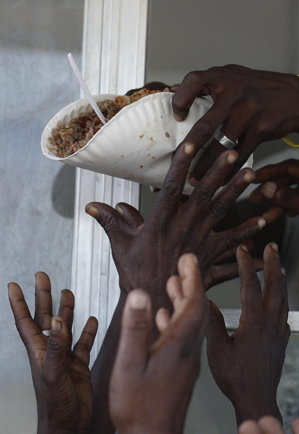 A man hands out a meal of beans and rice during a federal government distribution of food and school supplies to some residents of Cite Soleil, in Port-au-Prince, Haiti, Thursday, Oct. 3, 2019. The daily struggles of Haitians have only become more acute as recent anti-government protests and roadblocks force the closure of businesses, sometimes permanently, as people lose jobs and dwindling incomes fall behind a spike in prices. (AP Photo/Rebecca Blackwell)