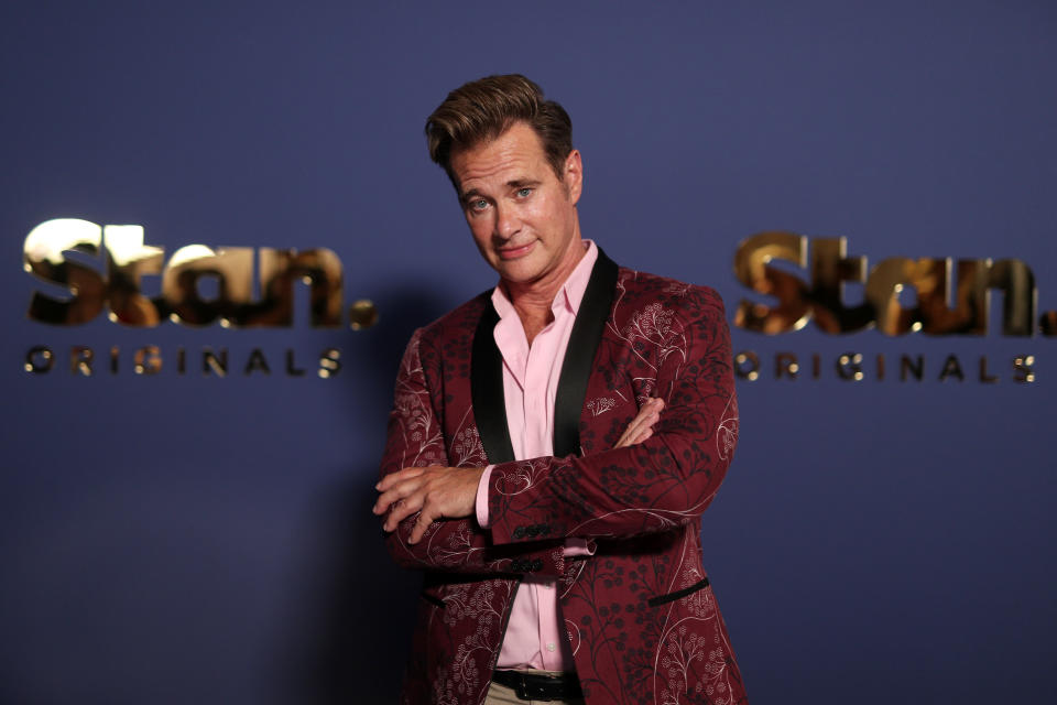 A photo of Richard Reid wearing a burgundy jacket on the Stan blue carpet.