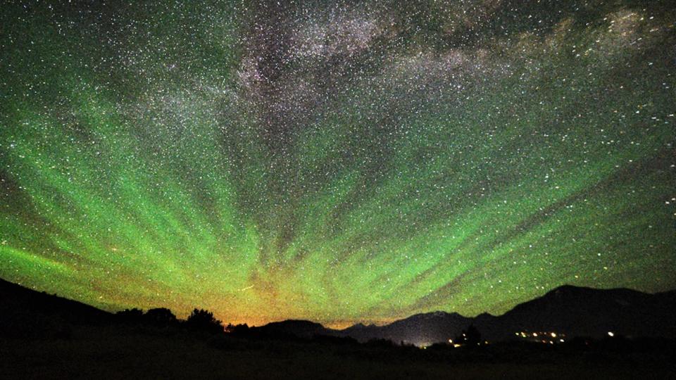 Green streaks of light shine in the night sky full of stars