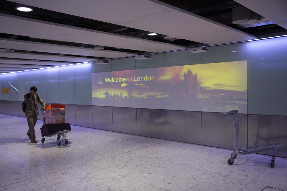 A man pushes luggage past a welcome to London sign at Heathrow Airport in London, Tuesday, Jan. 26, 2021, during England's third national lockdown since the coronavirus outbreak began. The British government are on Tuesday expected to discuss whether to force some travellers arriving in the UK to quarantine in hotels to try to curb the spread of coronavirus. (AP Photo/Matt Dunham)