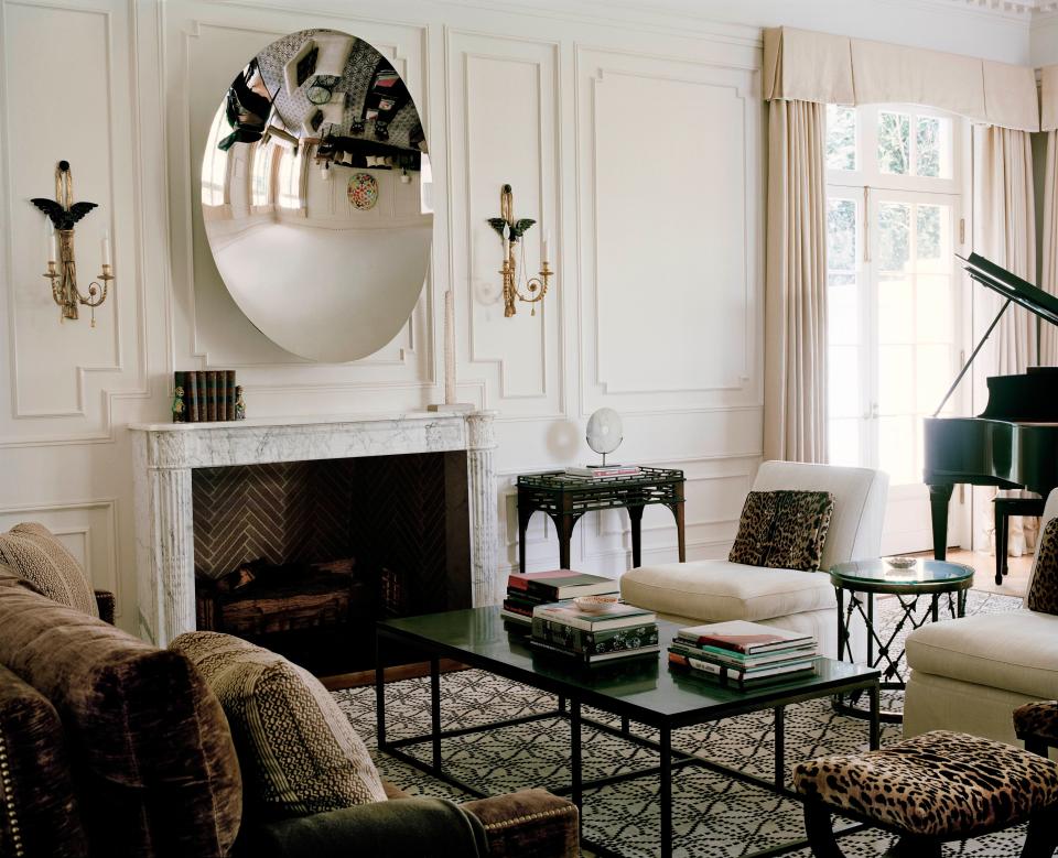 The living room, designed in the manner of Hollywood homes of the 1920s and ’30s, doubles as a screening room. A screen descends from the ceiling and speakers are hidden in the neoclassical, French-inspired paneling. The Anish Kapoor steel mirror, flanked by Federal period sconces and hanging above a Louis XVI marble fireplace mantel, reflects other collectibles around the room, such as Billy Baldwin slipper chairs sheathed in a Glant fabric and an Oscar de la Renta rug.