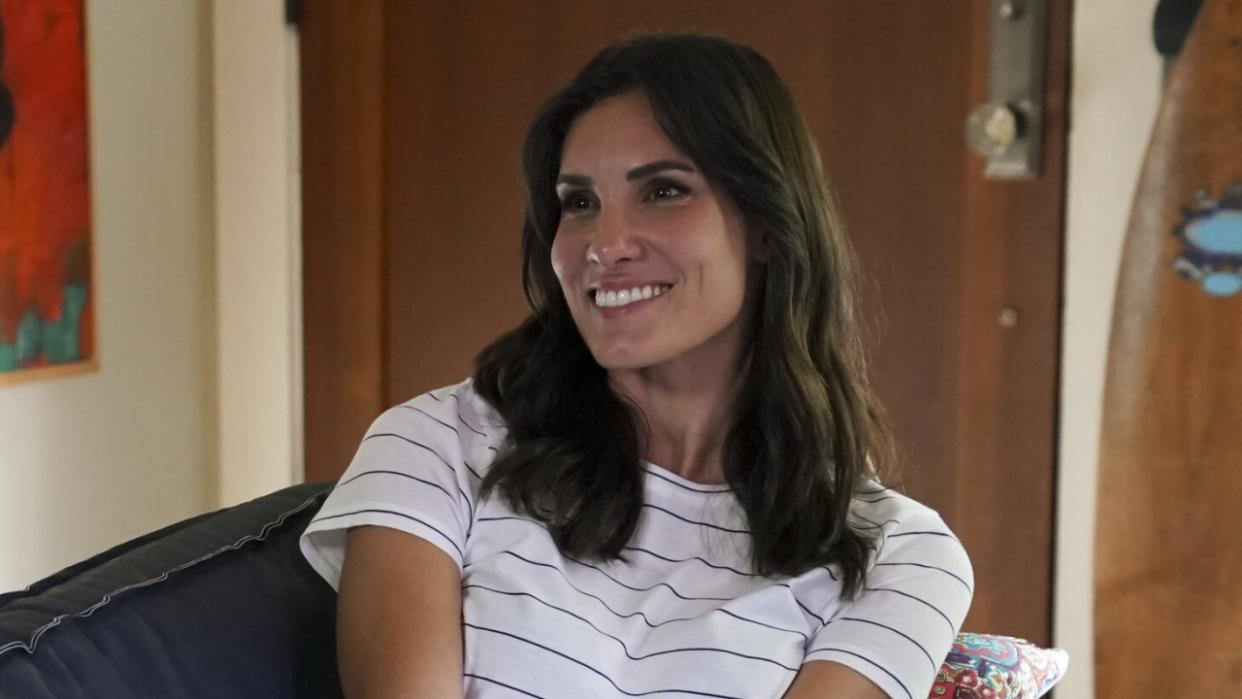  Kensi smiling on couch in striped shirt on NCIS: Los Angeles. 