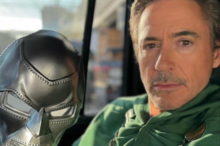 Robert Downey Jr. smirks as the camera while holding a Doom mask.