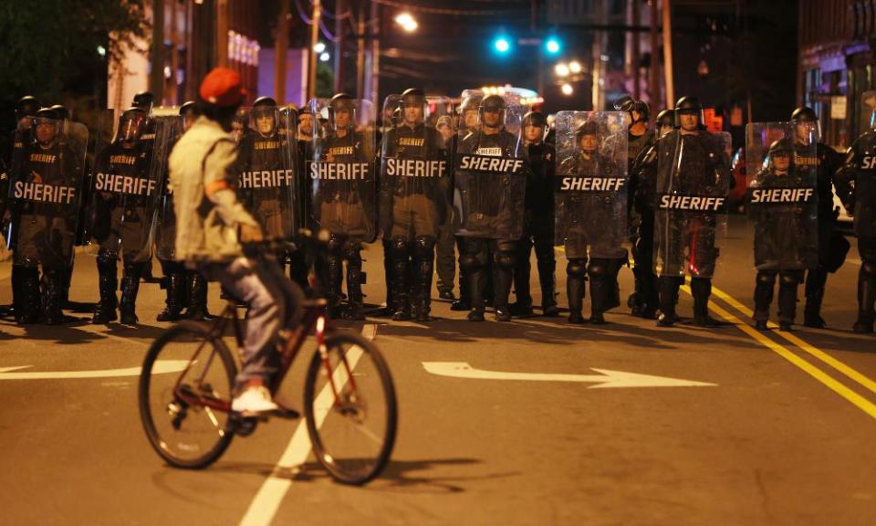 Law enforcement officials in riot gear block the street.