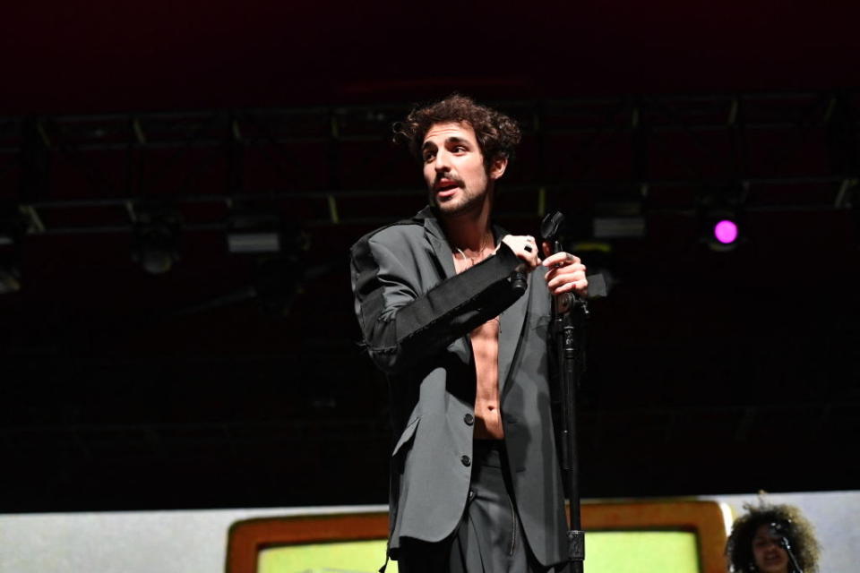 Saint Levant on stage holding a microphone stand, wearing an open, unbuttoned suit jacket