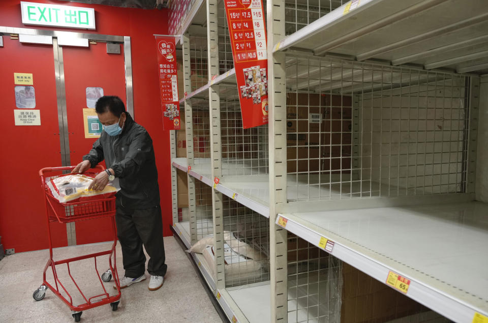 FILE - A man wearing a face mask gets a bag of rice at a grocery cart next to empty-looking shelves for rice after residents concerned with possible shortages stock up on food, at a supermarket Hong Kong on March 6, 2022. The fast-spreading omicron variant is overwhelming Hong Kong, prompting mass testing, quarantines, supermarket panic-buying and a shortage of hospital beds. Even the morgues are overflowing, forcing authorities to store bodies in refrigerated shipping containers. (AP Photo/Vincent Yu, File)