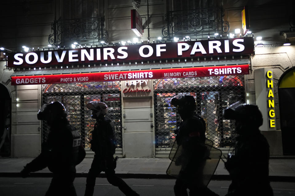 FILE - Police officers walk past a souvenir store in Paris, Saturday, July 1, 2023. President Emmanuel Macron on Saturday scrapped an official trip to Germany after a fourth straight night of rioting and looting across France in defiance of a massive police deployment. Hundreds turned out for the burial of the 17-year-old whose killing by police triggered the unrest. After more than 3,400 arrests and signs that the violence is now abating, France is once again facing a reckoning (AP Photo/Christophe Ena, File)