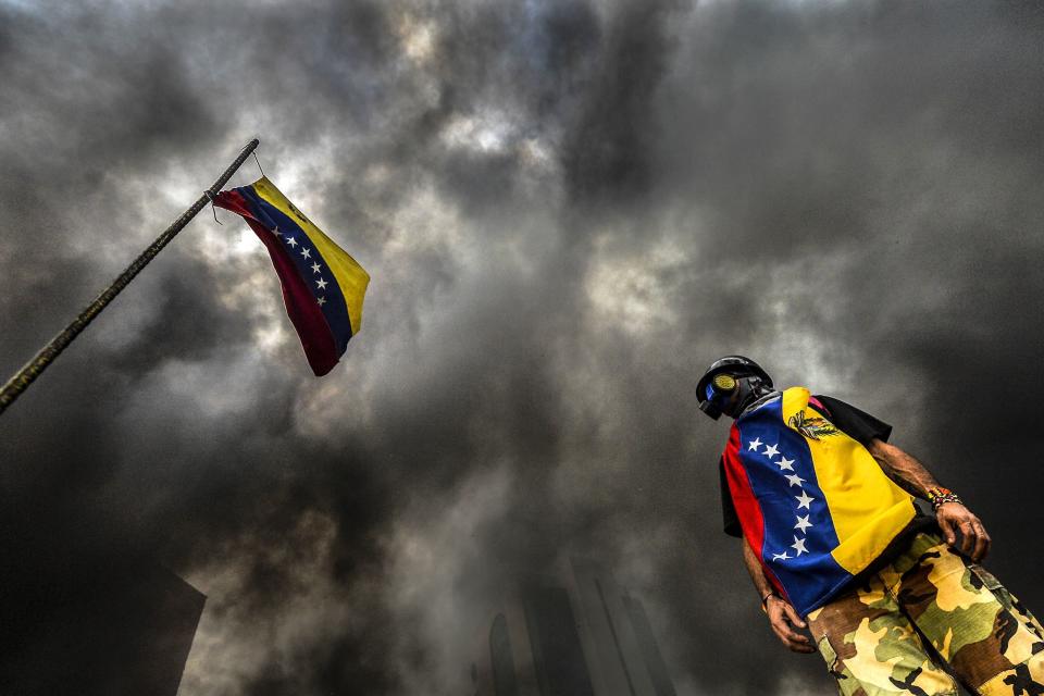 An anti-government demonstrator stands next to a national flag during an opposition protest blocking the Francisco Fajardo highway on May 27.