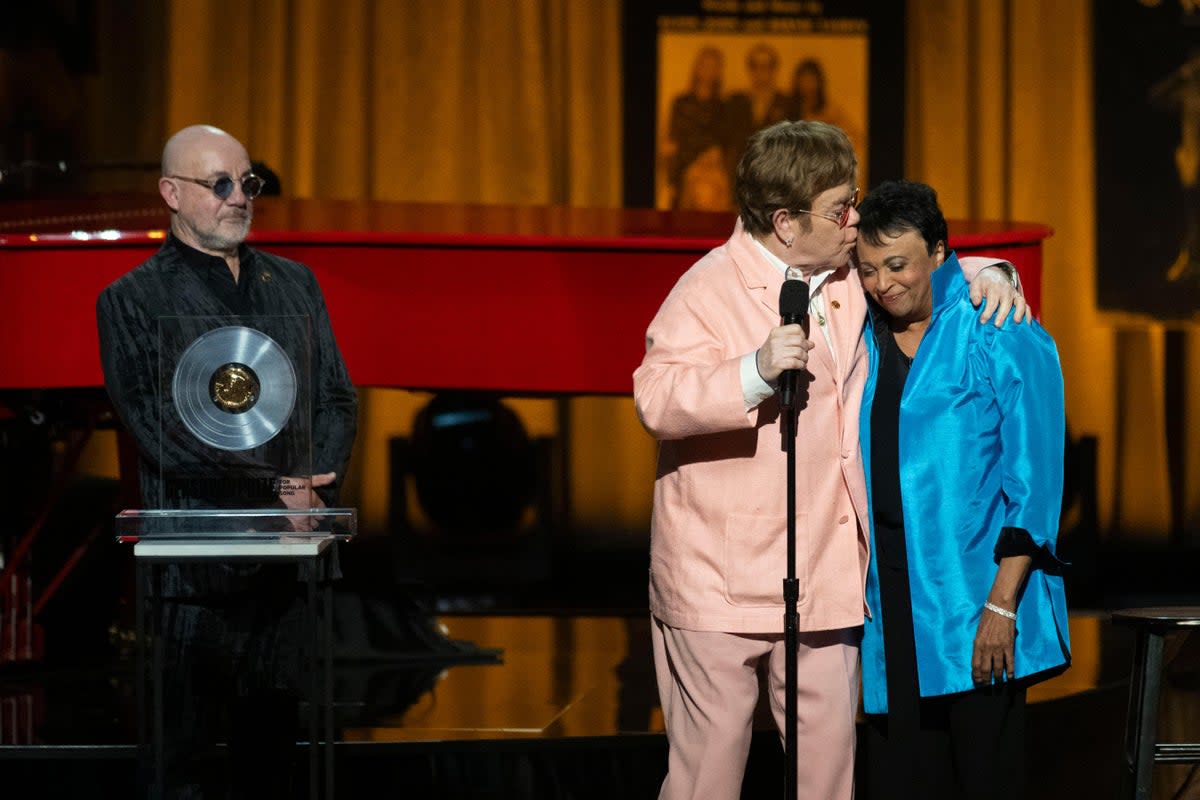 The singer, centre, collected the award together with his songwriting partner Bernie Taupin, left  (AP)