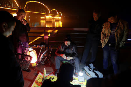 People gather around a fortune teller in front of the Broken and Friendship bridges across the Yalu River in Dandong, China's Liaoning province, March 30, 2017. REUTERS/Damir Sagolj