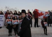 An ultra-Orthodox Jewish man walks past Israelis rallying to thank Canada's Prime Minister Stephen Harper for his support of Israel during his visit at the Israeli parliament in Jerusalem January 20, 2014. REUTERS/Ammar Awad (JERUSALEM - Tags: POLITICS)