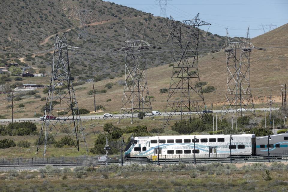 A white train is seen amid a landscape of brown hills with patches of shrubs