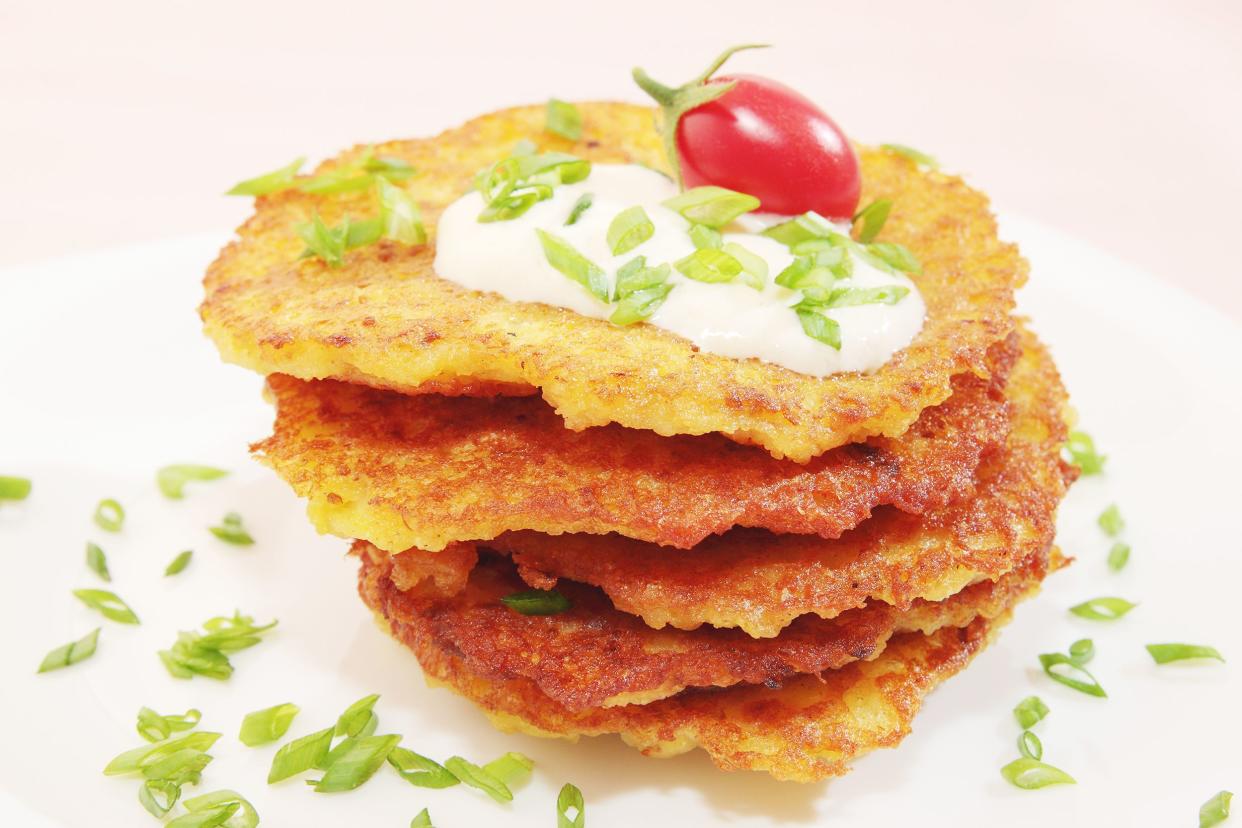 Stack of five german potato pancakes (Kartoffelpuffer) on a white plate with scallion garnish with a pink background