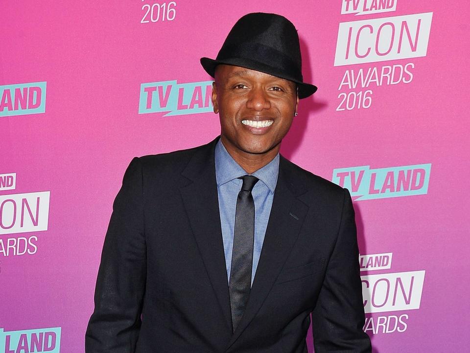 Javier smiling in a fedora, shirt, tie, and blazer in front of a backdrop.