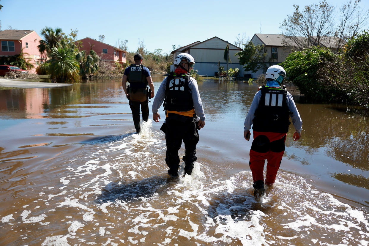 Helmeted members of the Texas A&M Task Force 1 Search and Rescue team stride through inches of water toward some houses.
