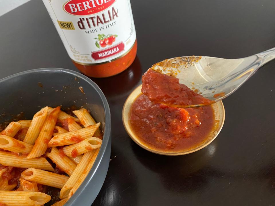 spoon showing close-up of bertolli pasta sauce with a bowl of pasta in background
