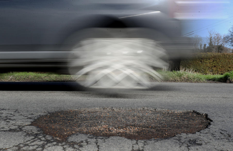 File photo dated 20/03/18 of a car passing a potholes. Councils should be given a five-year funding settlement to tackle the "national scandal" of potholes on England's local roads, according to MPs.