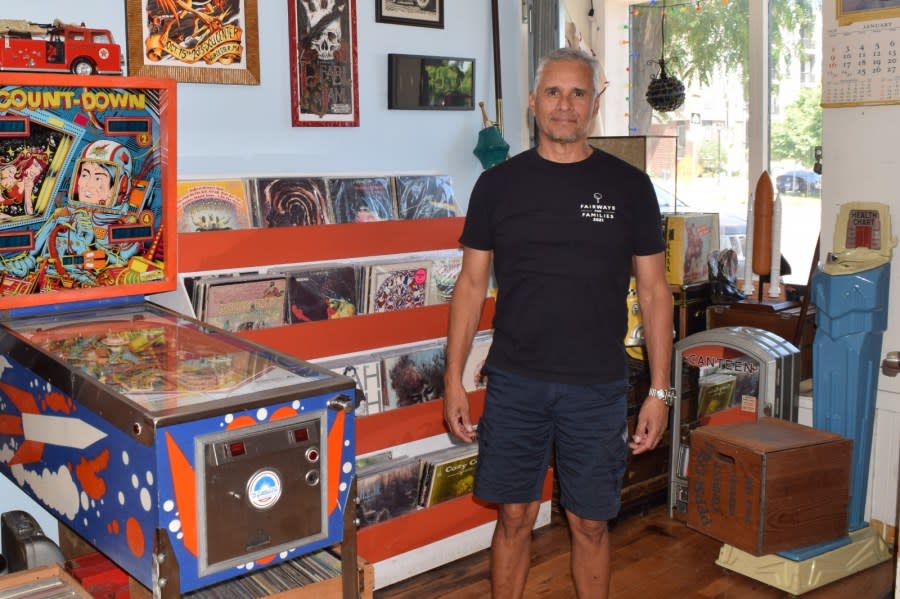 Peter Arguello in a shop with a pinball machine, stacks of records and other items