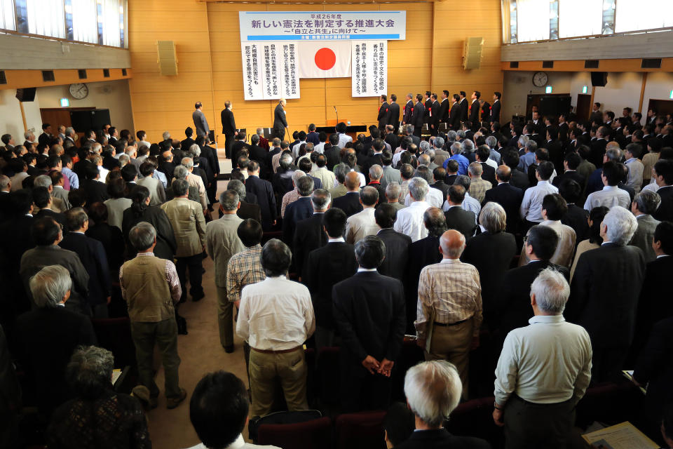 In this Thursday, May 1, 2014, guests and audience stand as they listen to the Japanese national anthem at a meeting of a pro-constitution amendment group in Tokyo. Japan is marking the 67th anniversary of its postwar constitution on May 3, 2014 with growing debate over whether to revise the war-renouncing document. Prime Minister Shinzo Abe’s ruling conservative party has long advocated revision but been unable to sway public opinion. Now he proposes that the government reinterpret the constitution so it can loosen the reins on its military without having to win approval for constitutional change. (AP Photo/Eugene Hoshiko)