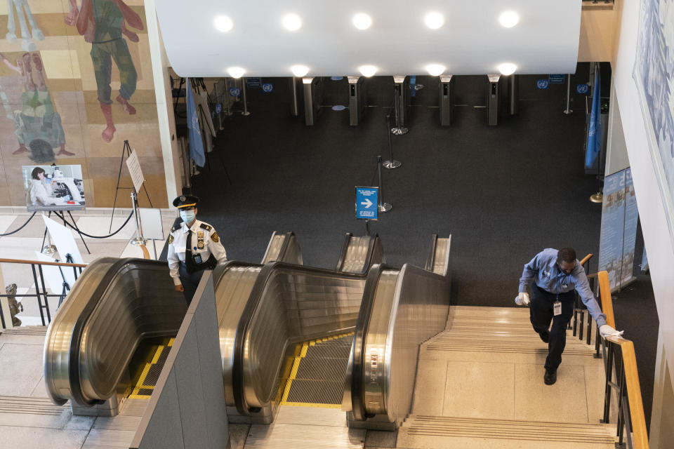 Un empleado de Naciones Unidas, derecha, desinfecta un pasamanos en la entrada para delegados, el lunes 21 de septiembre de 2020 en la sede de la ONU, en Nueva York. (AP Foto/Mary Altaffer)