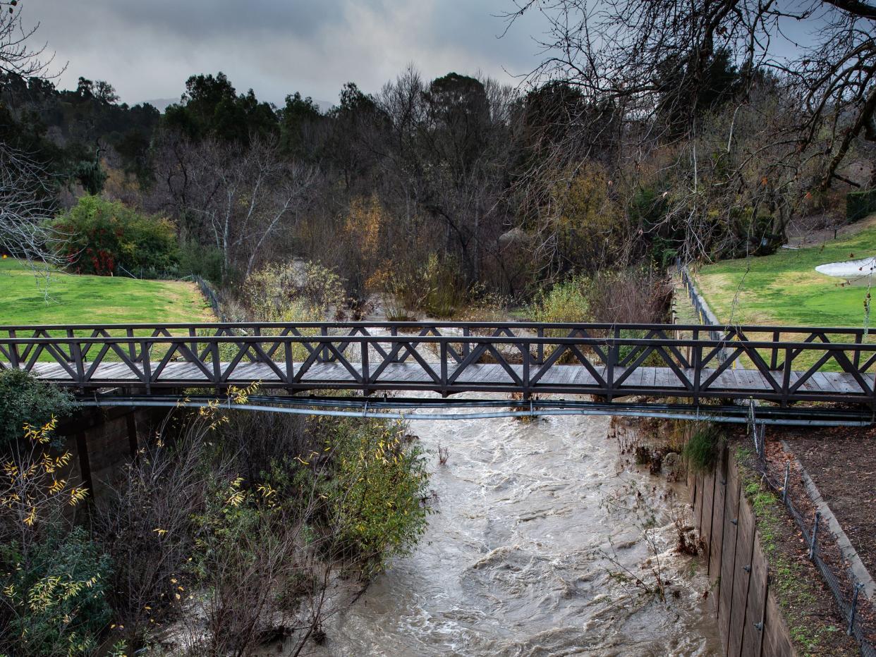 A large river full of brown water in between two cliffs with a bridge connecting the cliffs