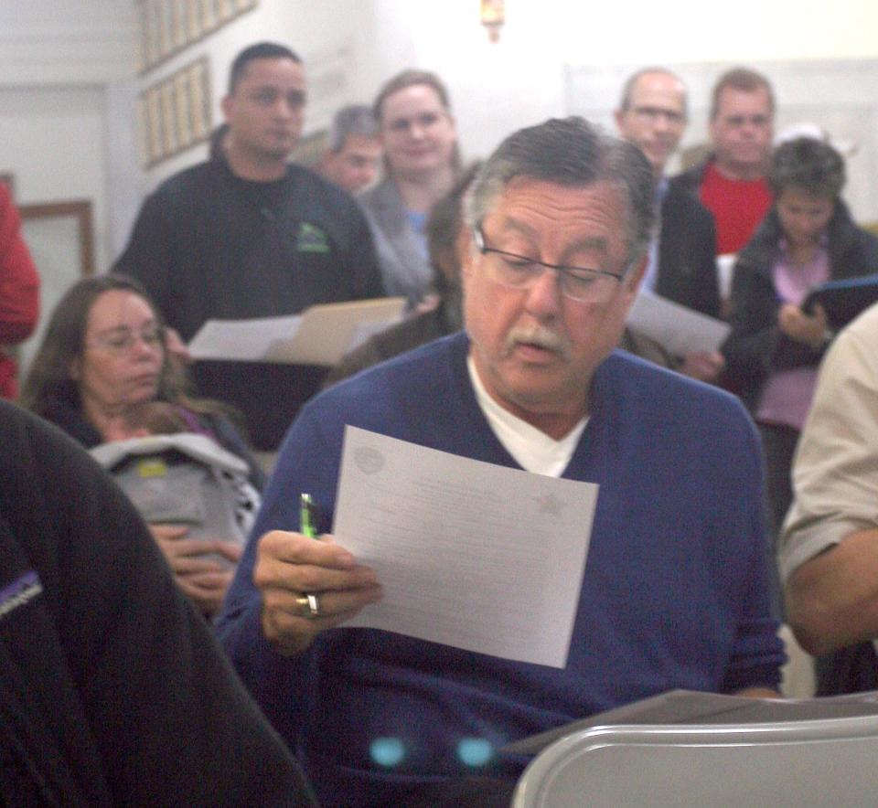 Landlord Gary Thomas fills out paperwork to bid on foreclosed properties at a Summit County sheriff's sale in 2018, where most of the auctioned properties were his. Patrick Bravo, executive director of the Summit County Land Bank, stands behind Thomas ready to outbid the landlord.