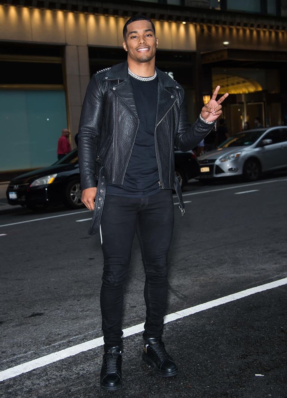 Rome Flynn poses in the middle of the street while holding up a peace sign with his hands.