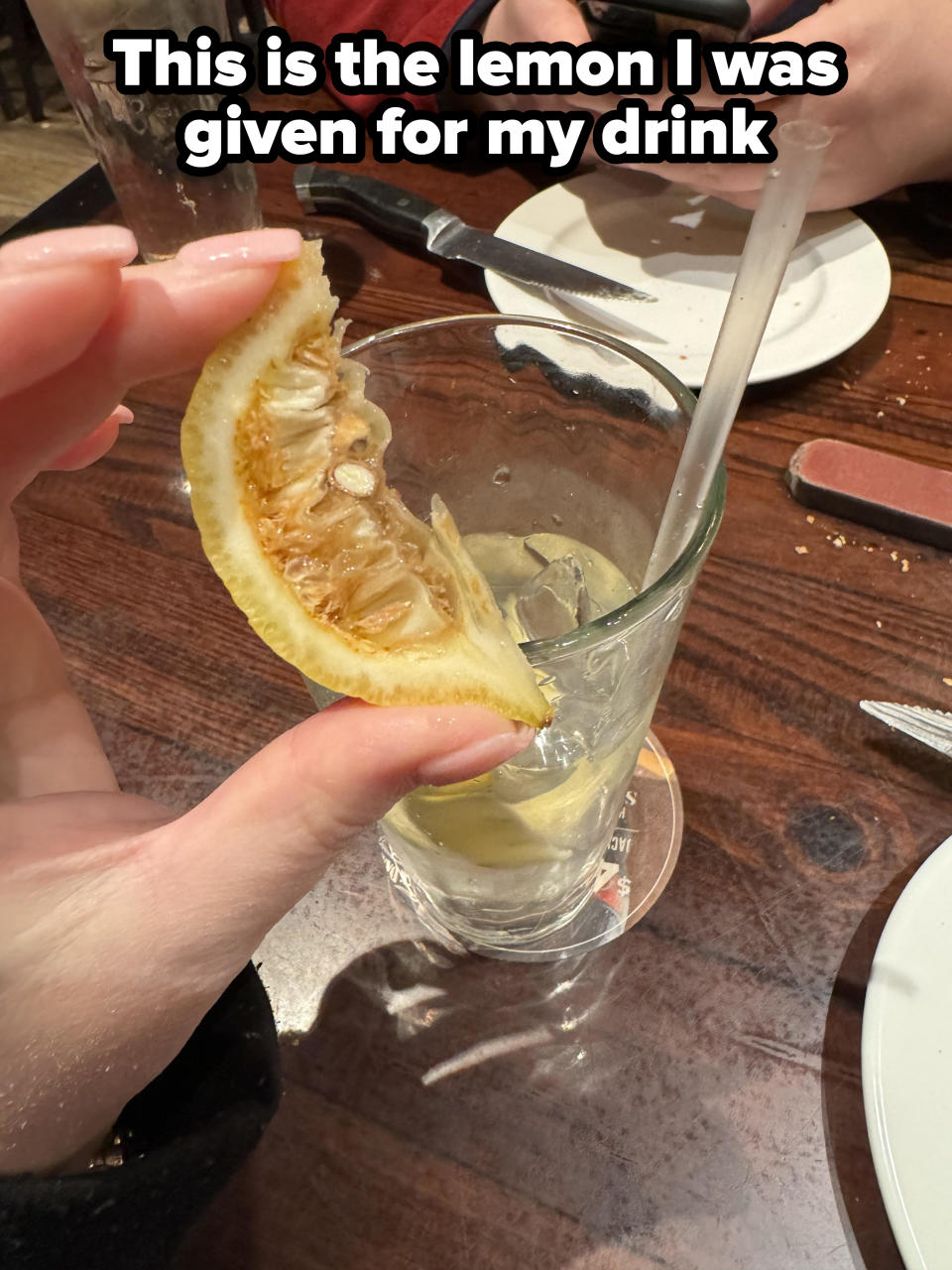 A person holds a desiccated, old lemon slice with caption "This is the lemon I was given for my drink"