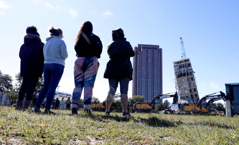 People gather to watch the demolition of the so called "Leaning Tower of Dallas" as a wrecking ball works to topple the structure north of downtown Dallas, Monday, Feb. 24, 2020. The still standing structure is part of an 11-story building that found a second life online after surviving a first demolition attempt. The former Affiliated Computer Services building inspired jokes and comparisons to Italy's Leaning Tower of Pisa when a Feb. 16 implosion failed to bring down its core. The company that engineered the blast said some explosives did not go off. (AP Photo/LM Otero)