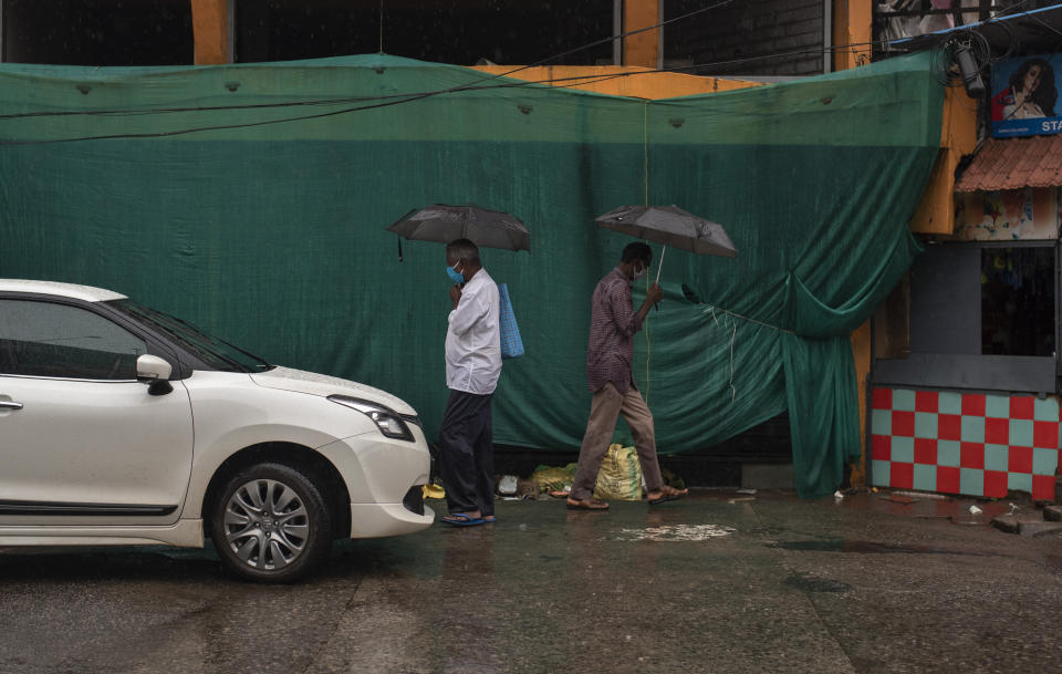 People wearing masks as a precaution against the coronavirus walk during rainfall in Kochi, Kerala state, India, Friday, Aug. 7, 2020. A mudslide triggered by heavy monsoon rain and flooding killed at least five people in the state on Friday, police said. (AP Photo/R S Iyer)