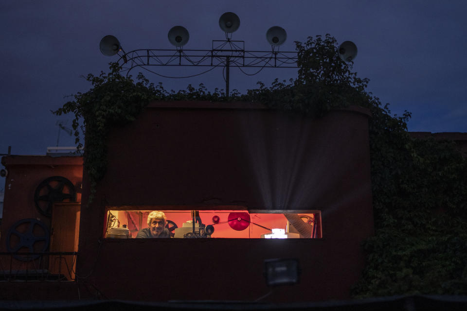 In this Saturday, May 30, 2020 photo, projector operator Pavlos Lepeniotis operates his equipment and peers out from the projection booth at the Zephyros open-air cinema that specializes in films from past decades in Athens' central Petralona district. (AP Photo/Petros Giannakouris)