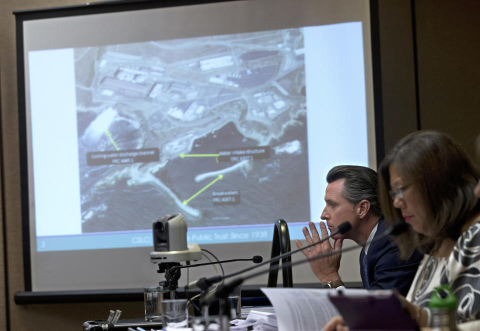 FILE - A photo of the Diablo Canyon Nuclear Power Plant is displayed at then-California Lt. Gov. Gavin Newsom, second from right, during discussion about a renewing the plant's license on June 28, 2016, in Sacramento, Calif. California's last operating nuclear power plant could get a second lease on life. Owner Pacific Gas & Electric decided six years ago to close the twin-domed power plant by 2025. But Democratic Gov. Newsom, who was involved in the agreement to close the reactors, has prompted PG&E to consider seeking a longer lifespan for the plant. (AP Photo/Rich Pedroncelli, File)