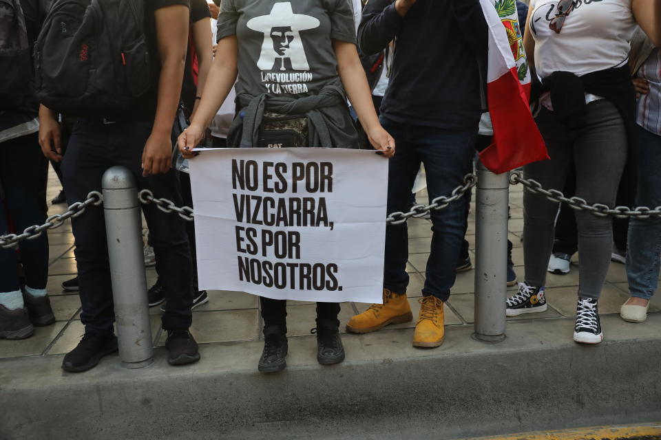 A woman, holding a sign with a message that reads in Spanish: "It's not for Vizcarra, it's for us," joins others outside the Justice Palace where people who are refusing to recognize the new government gathered to protest, in Lima, Peru, Wednesday, Nov. 11, 2020. On Tuesday, Peru swore in Manuel Merino as president, after Peru’s legislature booted President Martin Vizcarra from office on Monday. (AP Photo/Rodrigo Abd)