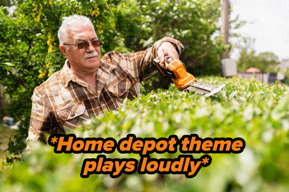 An older man in a plaid shirt uses an electric hedge trimmer to trim bushes in a garden