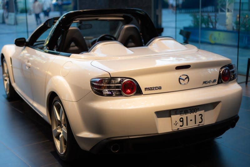 An image of the back of a white, roof-less Mazda RX-8 in one of the brand's showrooms.