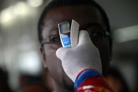 A health worker takes a passenger's temperature with an infrared digital laser thermometer at the Felix Houphouet Boigny international airport in Abidjan August 13, 2014. REUTERS/Luc Gnago