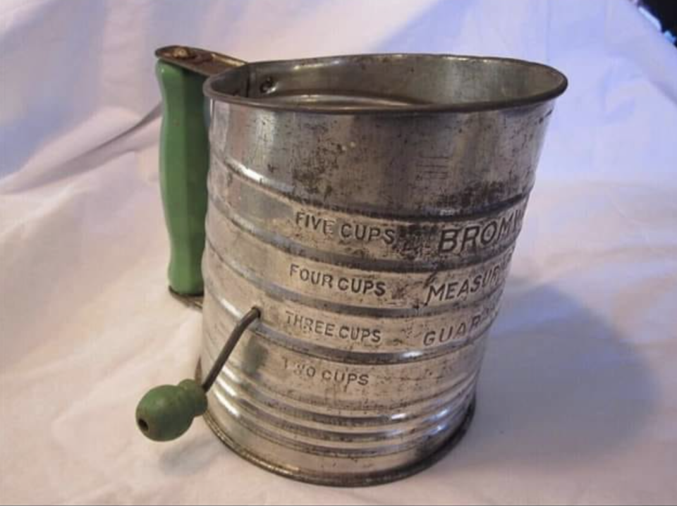A vintage metal flour sifter with measures (2–5 cups) and hand crank on the outside